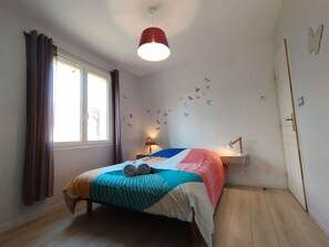 Een slaapkamer met een bed, een raam, gordijnen, een lamp en een muur versierd met vliegtuigstickers.