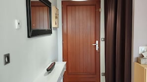 A hallway with a wooden door, a white console table with a remote control, a wall-mounted mirror, and a light fixture above the door. - 4-bed house with garden near Cahors, smart TV & Wii, peaceful and comfortable (Pradines)