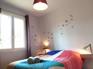 Ett sovrum med en säng, ett fönster, en lampa och väggdekorationer med fjärilsmotiv.
