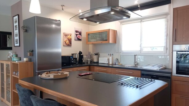 A modern kitchen with a central island, stainless steel appliances, wooden cabinets, and a window providing natural light. - 4-bed house with garden near Cahors, smart TV & Wii, peaceful and comfortable (Pradines)