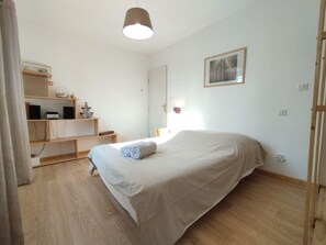 Ein Schlafzimmer mit einem Bett, einem Schreibtisch mit Computer, einem Regal mit Dekoration und einer Hängeleuchte.