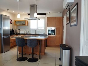 A modern kitchen with a central island, bar stools, stainless steel appliances, and wooden cabinets. - 4-bed house with garden near Cahors, smart TV & Wii, peaceful and comfortable (Pradines)