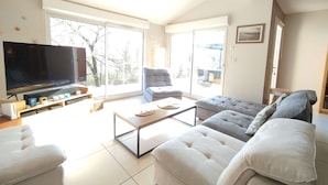 A spacious living room with a large flat-screen TV, a sofa set, a coffee table, and a sliding glass door leading to an outdoor area. - 4-bed house with garden near Cahors, smart TV & Wii, peaceful and comfortable (Pradines)