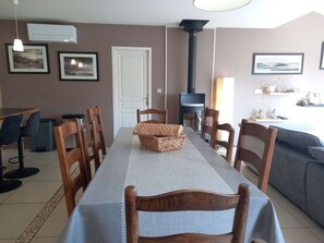 Een eetruimte met een lange tafel, stoelen, een rieten mand en een open haard.