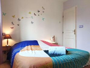Een slaapkamer met een bed, nachtkastje, lamp, deur en vlinderstickers op de muur.