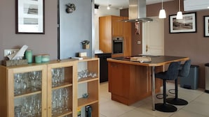 A compact kitchen with wooden cabinets, a built-in oven, and a central island with bar stools. - 4-bed house with garden near Cahors, smart TV & Wii, peaceful and comfortable (Pradines)
