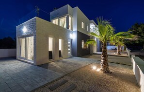 Ein modernes, zweistöckiges Haus mit großen Fenstern und gut ausgeleuchteter Fassade bei Nacht.