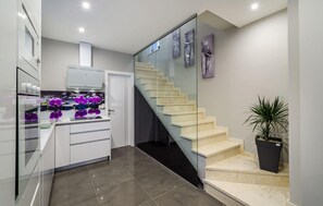 A modern kitchen with a glass island, a staircase with glass railings, and a potted plant. - Beautiful home in Zaton (Zaton)