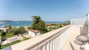 Ein Balkon mit Meerblick, ein weißes Gebäude und ein Baum.