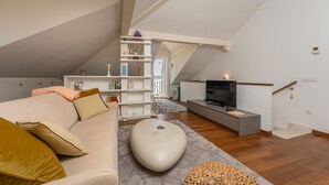 Ein modernes Wohnzimmer im Loft-Stil mit hohen Decken, einer Couch, einem Fernseher und einem Bücherregal.