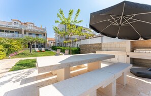 An outdoor patio with a table and benches, a grill, and a large umbrella. - Beautiful apartment in Biograd (Biograd)