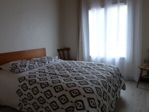 A bedroom with a bed, a wooden headboard, a chair, and a window with curtains. - Renovated house near beach, with parking, ideal for 4/6 people (La Tranche-sur-Mer)