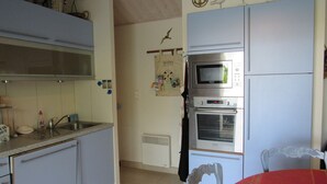 Une cuisine compacte équipée d’un évier, d’un four à micro-ondes et d’un réfrigérateur. On y trouve une chaise et une table recouverte d’une nappe colorée.