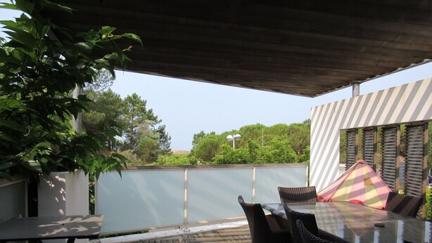 Une terrasse extérieure avec une table et des chaises, un auvent à rayures et une vue sur la verdure et les arbres.