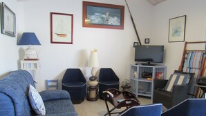 Un salon avec un canapé bleu, deux fauteuils, un téléviseur et des tableaux encadrés accrochés au mur.