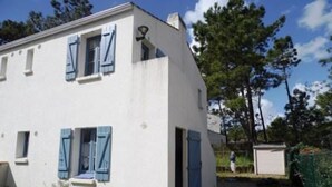 Een wit gebouw met blauwe luiken, een grindpad en een groene hek.