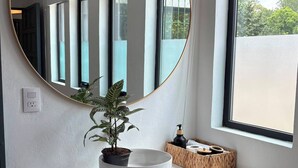 A bathroom vanity with a round mirror, a potted plant, a soap dispenser, and a small shelf. - Casa Puerto Siete8 (Mexico City)
