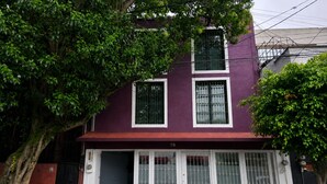 A two-story building with a purple facade, numbered 78, featuring a gated entrance with glass doors and windows, surrounded by trees. - Casa Puerto Siete8 (Mexico City)