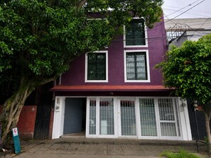 A two-story building with a purple facade, numbered 78, featuring a gated entrance with glass doors and windows, surrounded by trees. - Casa Puerto Siete8 (Mexico City)