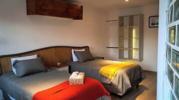 Een slaapkamer met twee bedden, een nachtkastje, een rode deken, een houten hoofdbord, een wandplank en een raam met gordijnen.