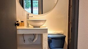 A bathroom with a round mirror, white sink, and blue toilet. - Casa Puerto Siete8 (Mexico City)