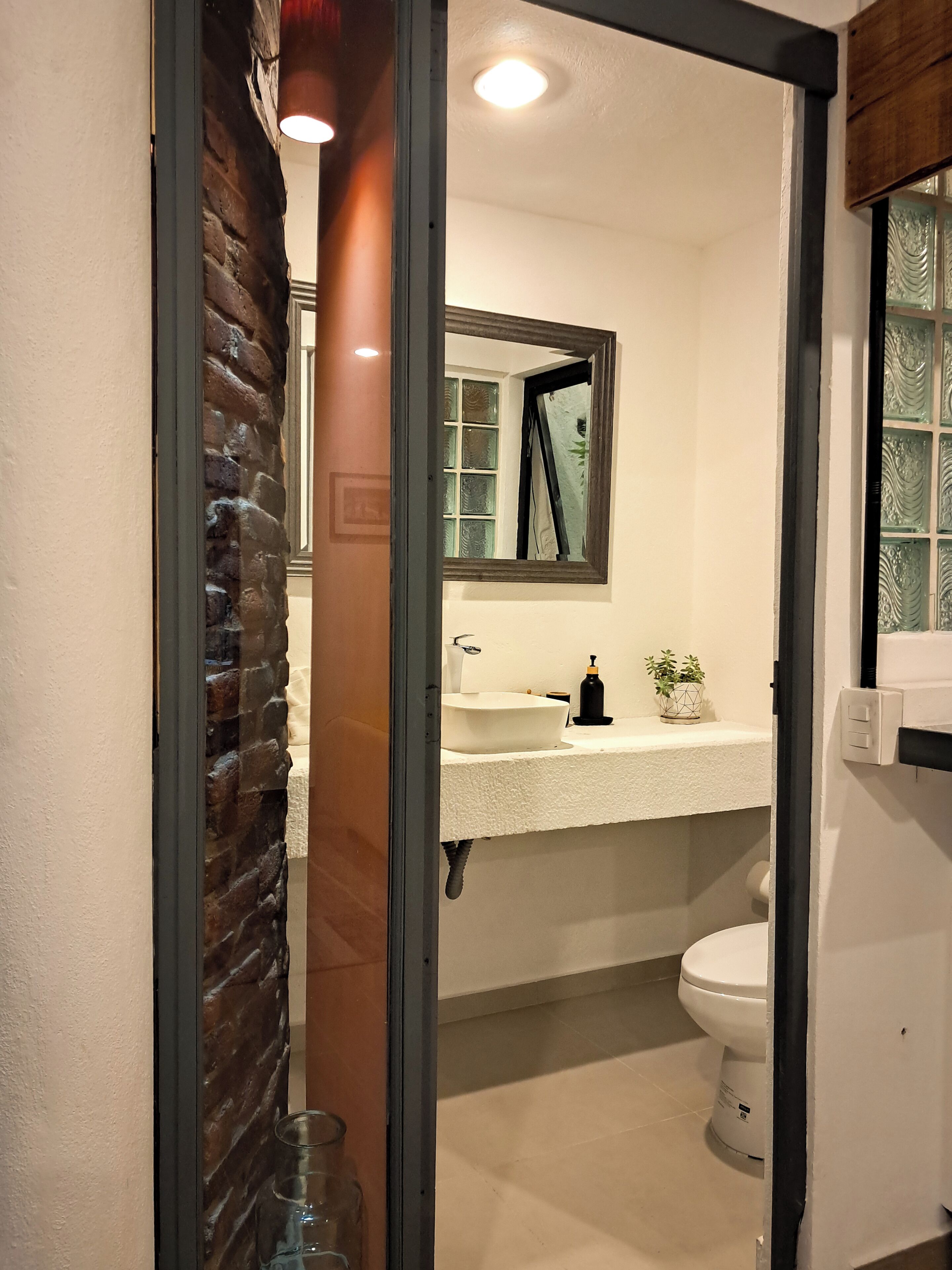 A bathroom with a white sink, a mirror, a toilet, and a window with decorative glass.