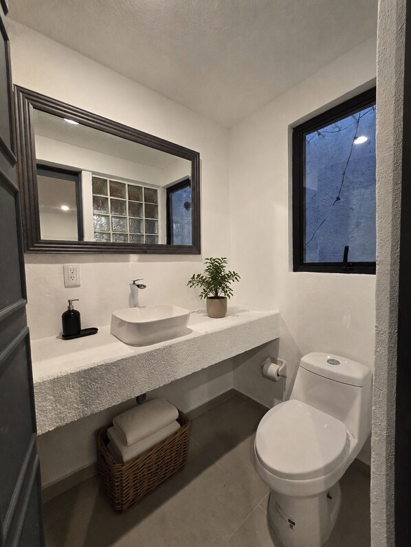 Ein Badezimmer mit einem weiĂen Waschbecken, einem Spiegel, einer Toilette und einem Fenster.