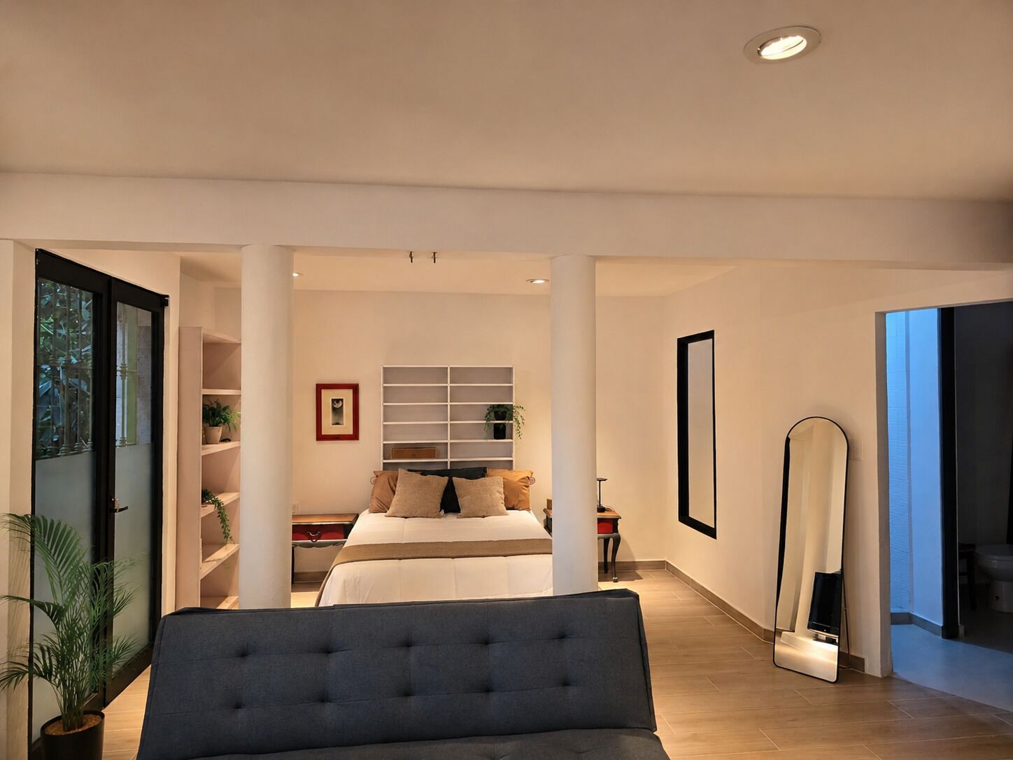 Un dormitorio moderno con una cama, un sofá, un espejo grande y una estantería.