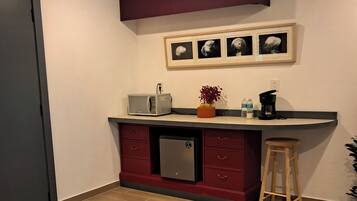 Una cocina compacta equipada con microondas, tostadora y cafetera, un taburete pequeño y una mesa de vidrio con alfombra.