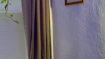 A bathroom with a shower curtain, a framed picture on the wall, a towel rack, and a small table with a bottle.