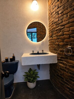 A bathroom with a round mirror, a sink, a toilet, and a potted plant. - Casa Puerto Siete8 (Mexico City)
