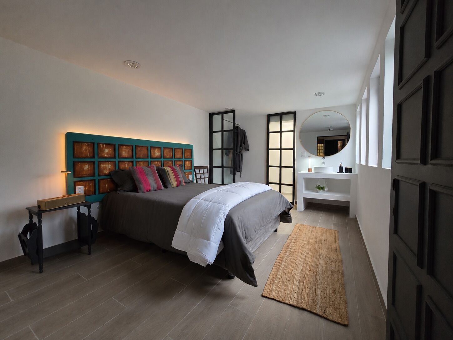 Un dormitorio moderno con una cama, una mesita de noche, un espejo y una lámpara de pared.