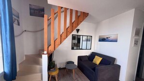 Un salon avec un escalier en bois, un canapé, une petite table et une plante en pot.