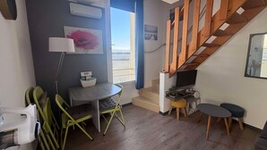 Un espace de vie compact comprenant un escalier en bois, une petite table avec une lampe, une chaise, un canapé et un téléviseur posé sur un meuble.