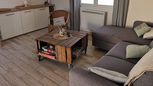 Ett mysigt vardagsrum med en soffa, ett soffbord med brädspel, en fåtölj i rotting och en tv som är monterad på väggen.