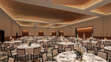 Un amplio salón de banquetes con varias mesas redondas dispuestas para comer, con un techo alto de listones de madera e iluminación empotrada.