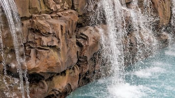 A man and a woman in a pool with a waterfall feature.