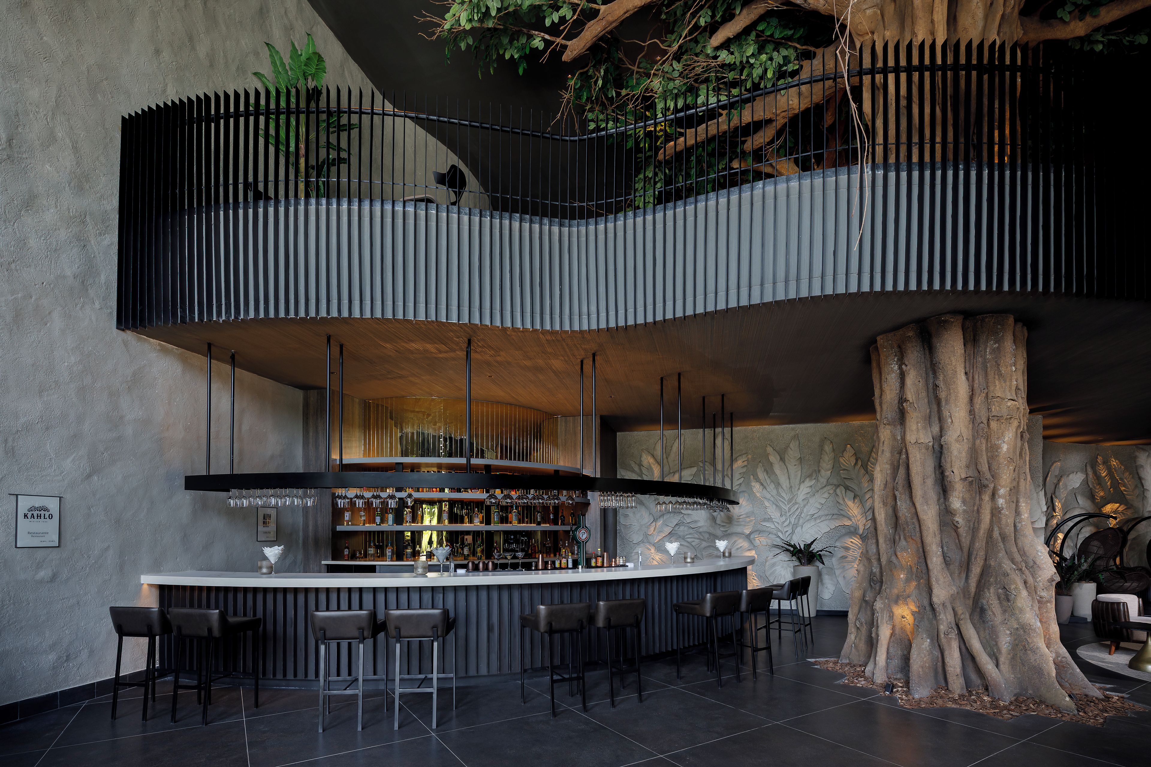 Un'area bar moderna con un bancone centrale, diverse opzioni di seduta e un'imponente struttura a forma di tronco d'albero.