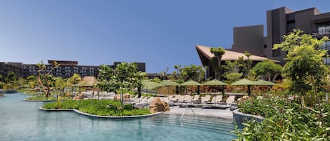 A resort pool area with clear water, lounge chairs, umbrellas, and a modern building in the background.
