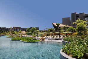 A resort pool area with clear water, lounge chairs, umbrellas, and a modern building in the background. - Lopesan Caoba Lagoon Resort Spa & Casino - All Inclusive (Punta Cana)