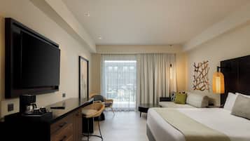 Une chambre d’hôtel dotée d’un grand téléviseur à écran plat, d’un bureau avec une machine à café, d’un fauteuil confortable, d’un lit avec des oreillers et d’une grande fenêtre avec des rideaux.