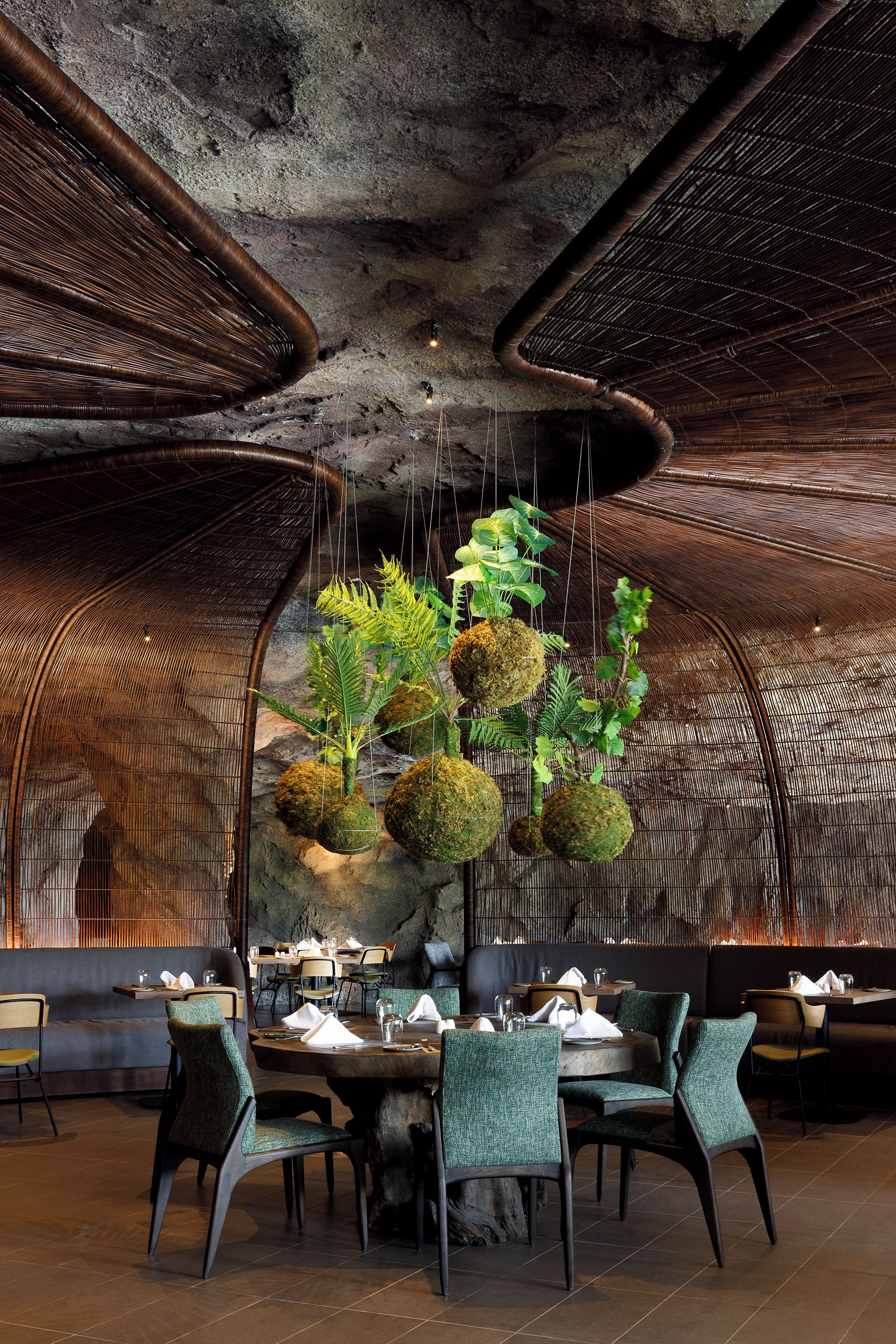 A restaurant interior with a unique ceiling design, hanging plants, and a rustic stone wall.