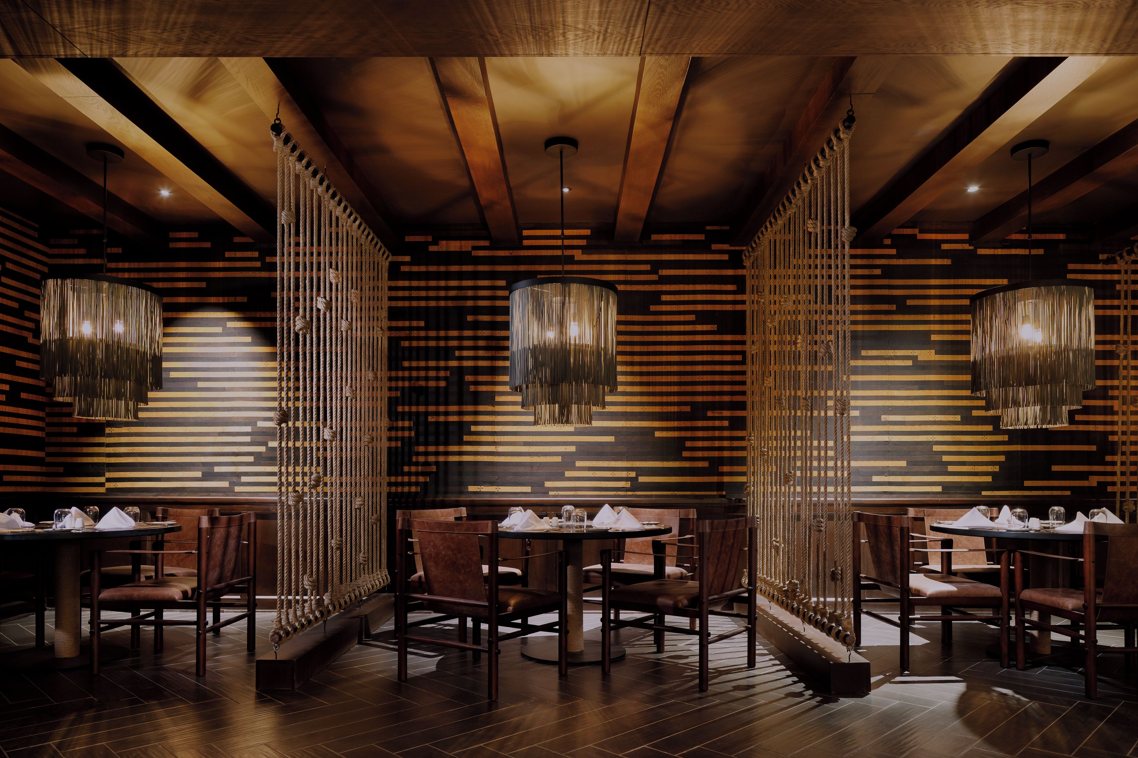 Un interno ristorante con pareti in legno a pannelli, decorazioni di corde appese e tavoli rotondi con sedie.