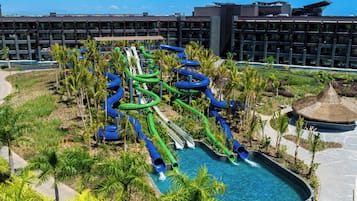 Un parc aquatique doté de nombreux toboggans et d’un espace piscine entouré de palmiers, avec un hôtel en arrière-plan.