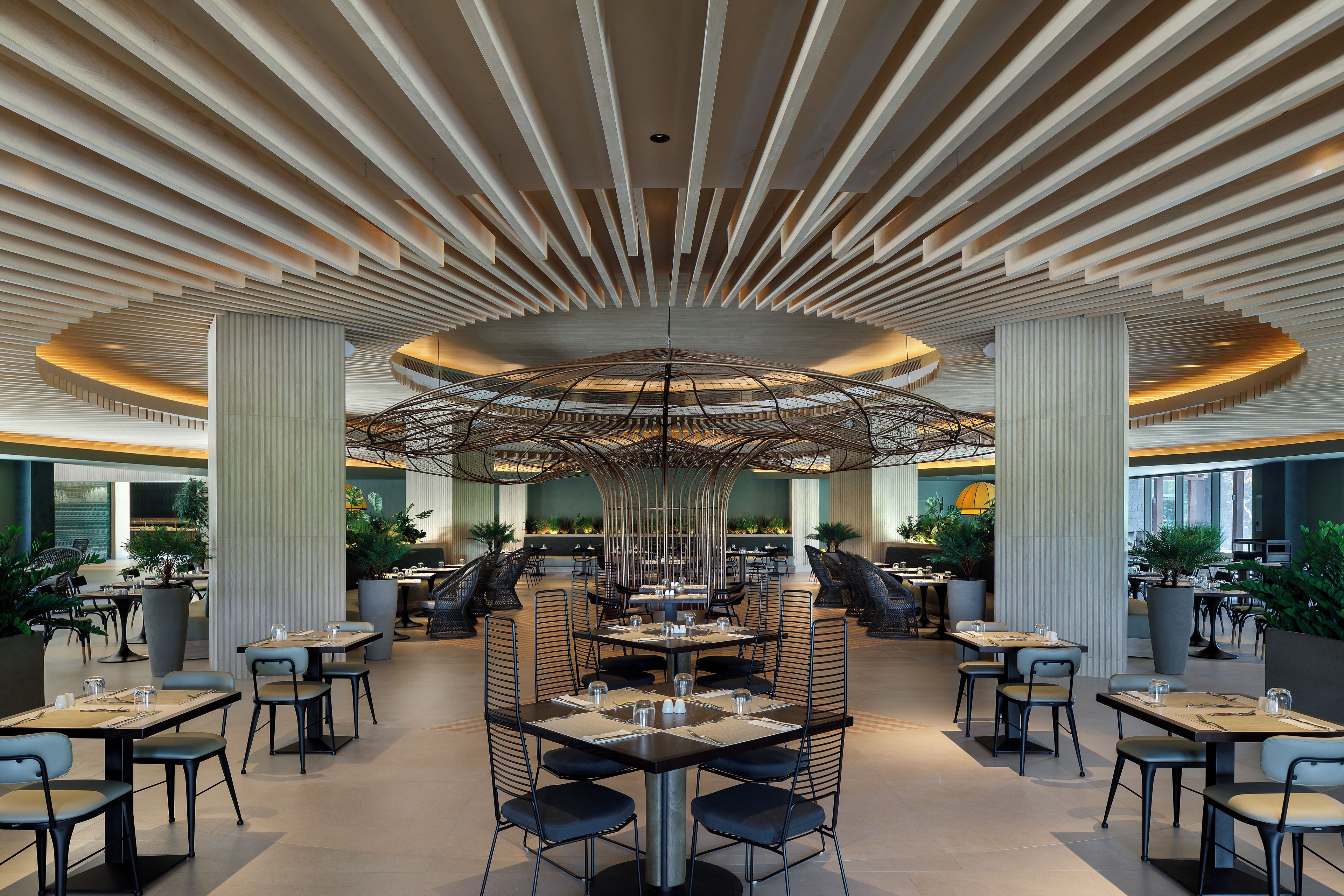 A spacious indoor area with multiple dining tables and chairs, a central decorative structure, and a modern ceiling design.