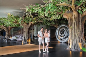 A modern indoor space with artificial trees and a spiral staircase. - Lopesan Caoba Lagoon Resort, Spa & Casino (Punta Cana)