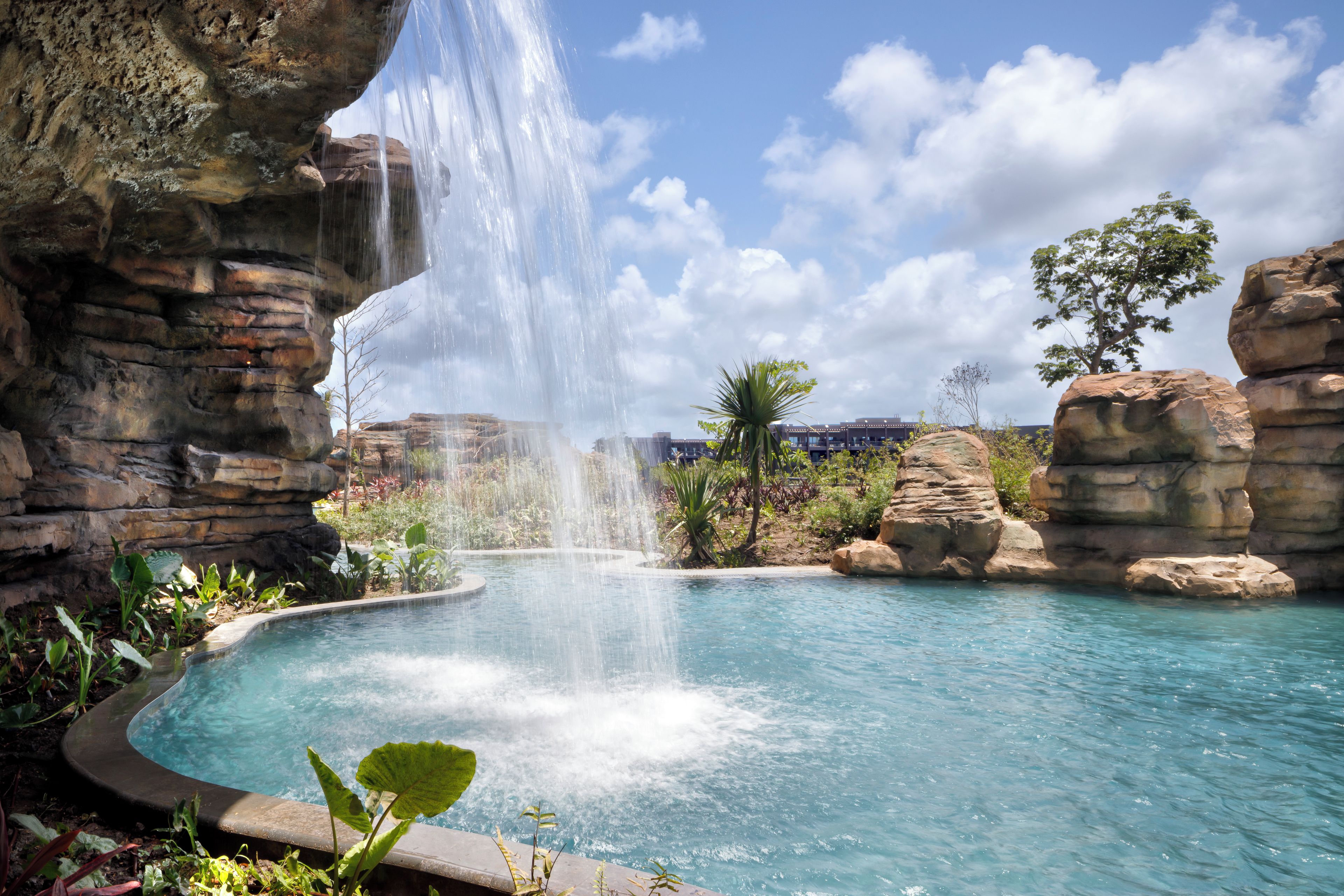 Une piscine agrémentée d’une cascade, entourée de formations rocheuses et de verdure.
