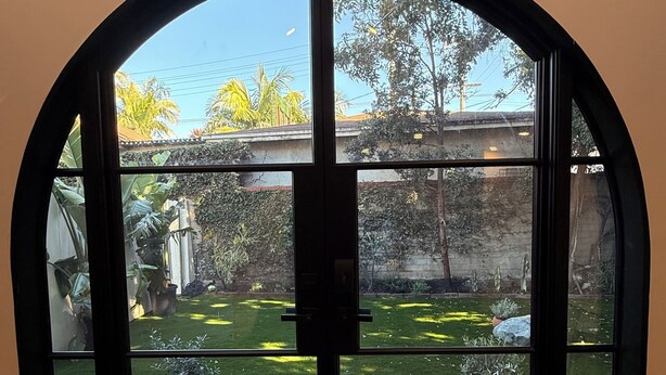 A view through a large arched window with a concrete floor and potted plants outside. - Brand New Moderne house with Private Garden Prime LA Location (Los Angeles)