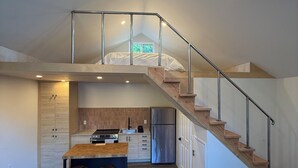 A modern kitchen with a central island, a dining area with stools, a black leather couch, and a staircase leading to an upper level. - Brand New Moderne house with Private Garden Prime LA Location (Los Angeles)