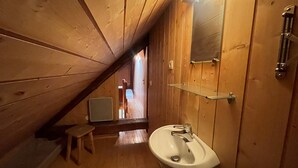 Un interno in legno con un soffitto spiovente, un lavandino bianco e uno specchio.